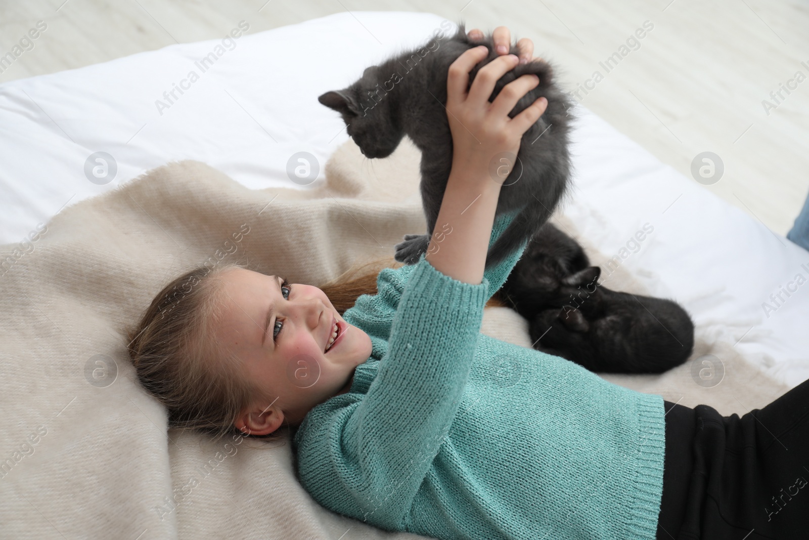 Photo of Little girl with cute fluffy kittens on bed indoors