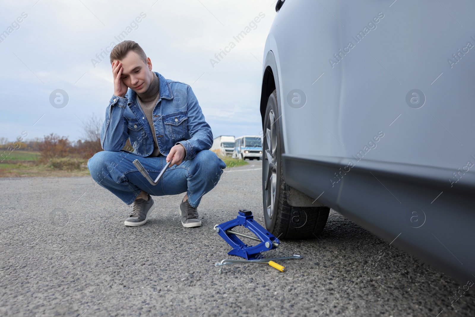 Photo of Worried young man near car with punctured wheel on roadside