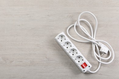 Photo of Power strip with extension cord on white wooden floor, top view. Space for text