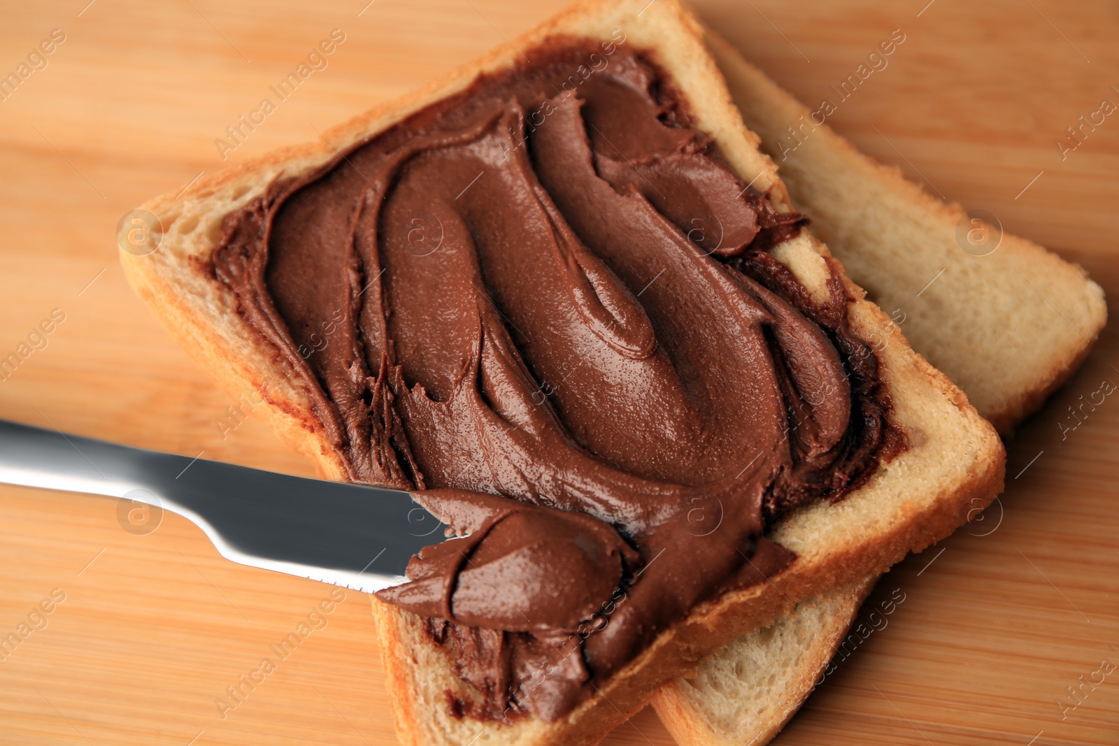 Photo of Tasty toast with chocolate paste and knife on wooden table, closeup