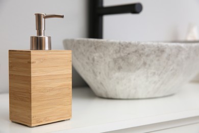 Wooden dispenser of liquid soap near sink in bathroom. Space for text