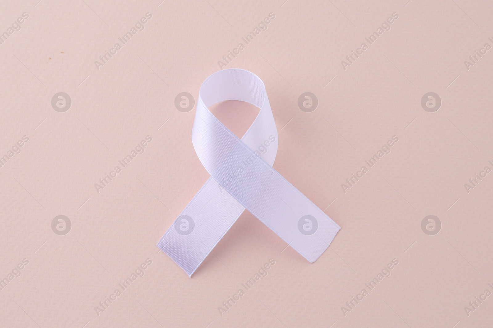 Photo of White awareness ribbon on beige background, top view