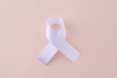 White awareness ribbon on beige background, top view