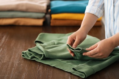 Photo of Woman folding clothes at wooden table indoors, closeup