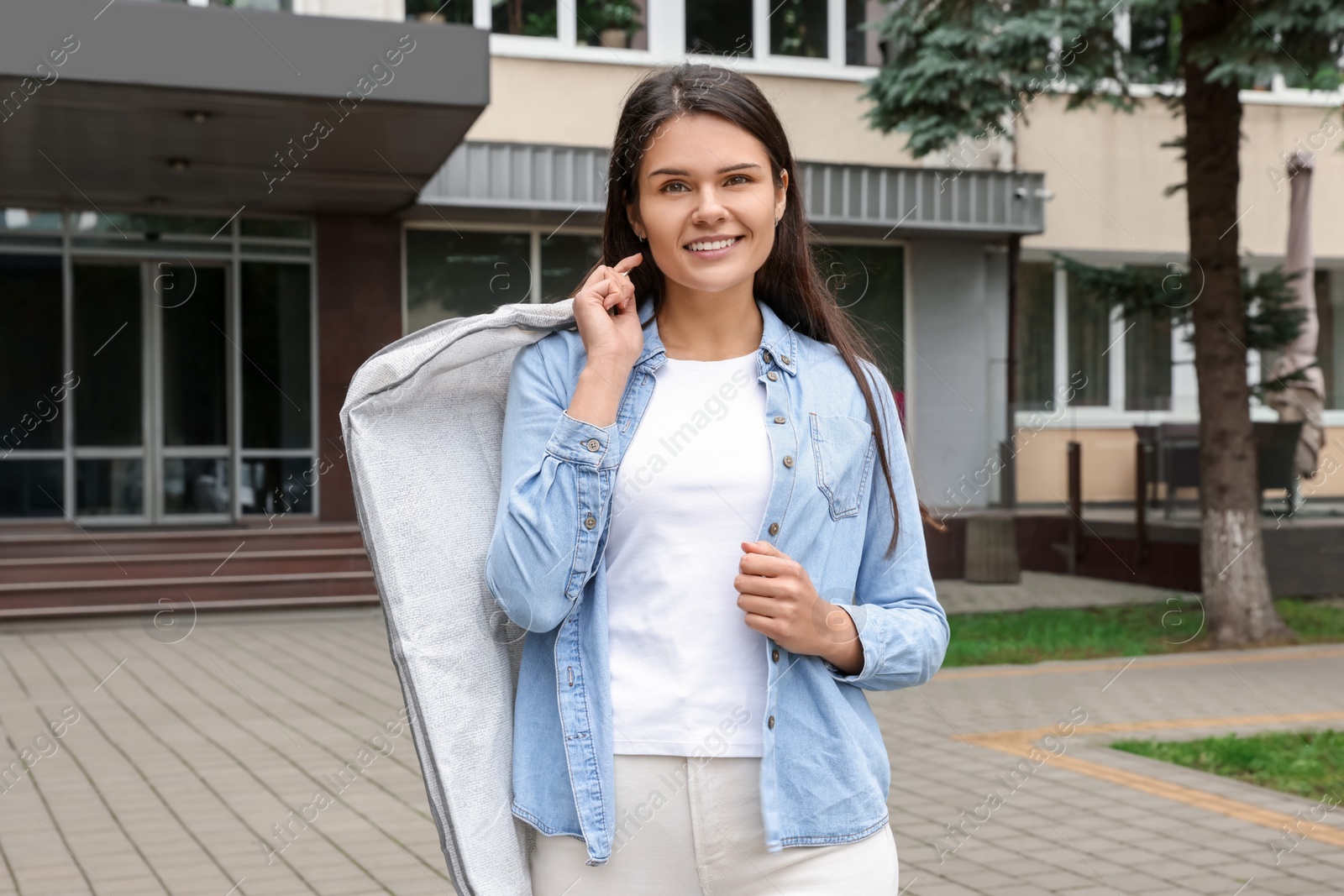 Photo of Attractive happy woman holding garment cover with clothes outdoors. Dry cleaning service