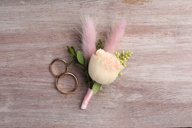 Small stylish boutonniere and rings on light wooden table, top view