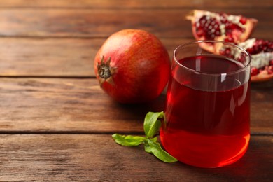 Photo of Tasty pomegranate juice in glass and fresh fruits on wooden table, closeup. Space for text