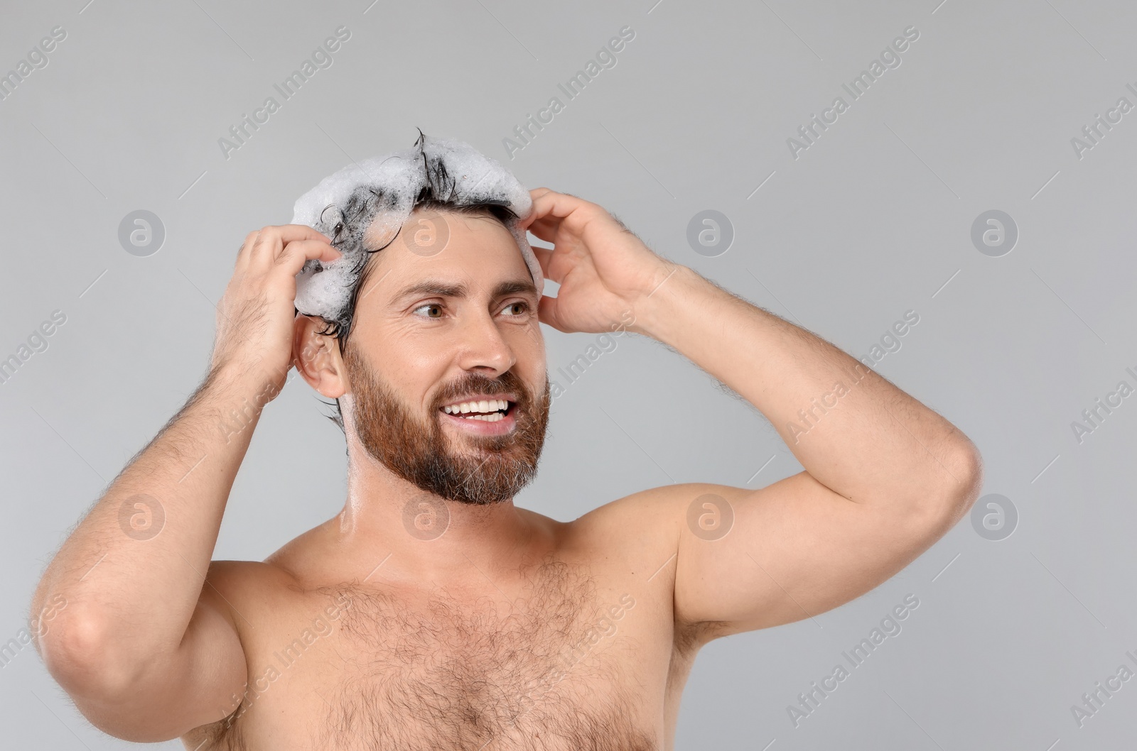 Photo of Happy man washing his hair with shampoo on grey background