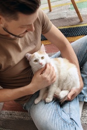 Photo of Young man with cute cat sitting on floor at home