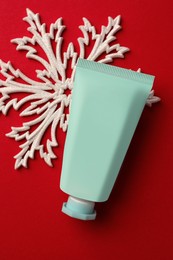 Photo of Tube of hand cream and snowflake on red background, flat lay. Winter skin care