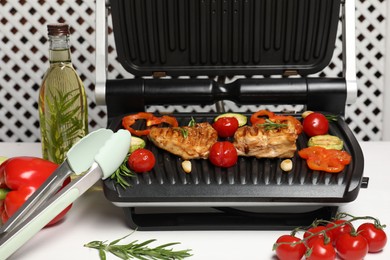 Electric grill with different products and tongs on white table