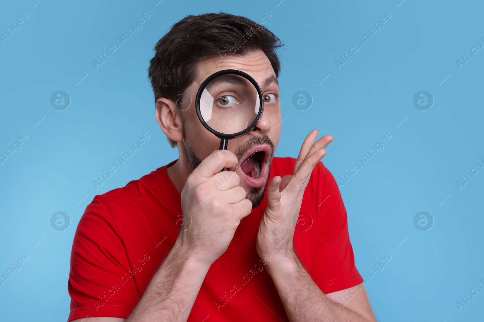 Photo of Emotional man looking through magnifier glass on light blue background