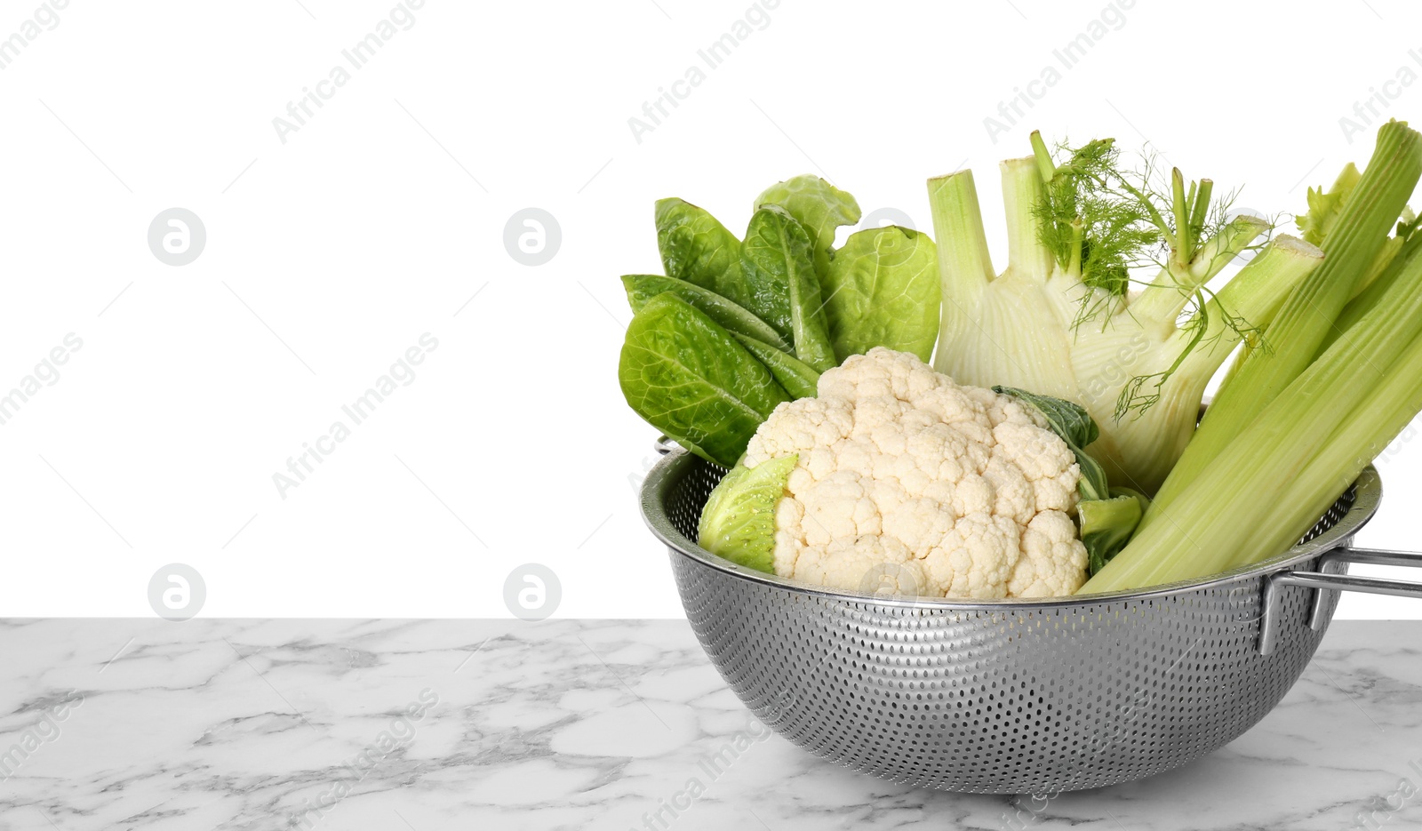 Photo of Metal colander with different vegetables on marble table against white background, space for text