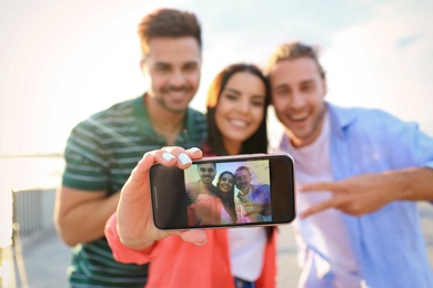 Happy young people taking selfie outdoors, focus on smartphone