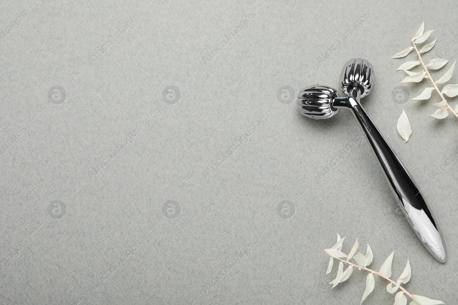 Photo of Metal face roller and leaves on grey background, flat lay. Space for text