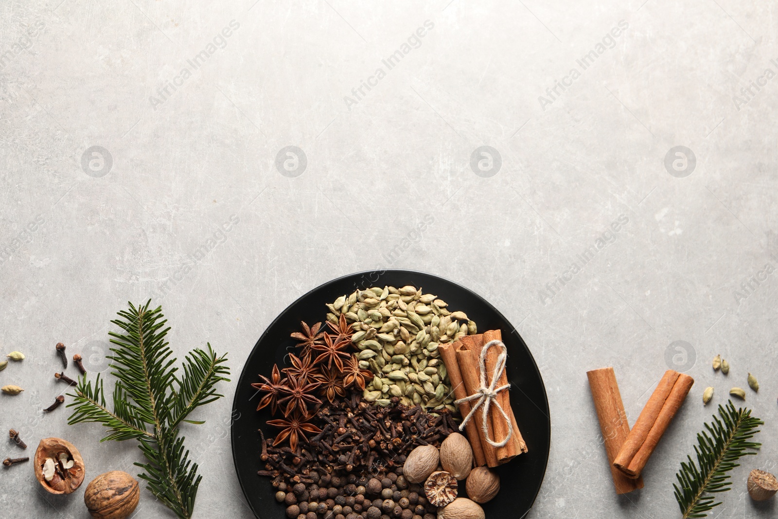 Photo of Different spices, nuts and fir branches on light gray textured table, flat lay. Space for text