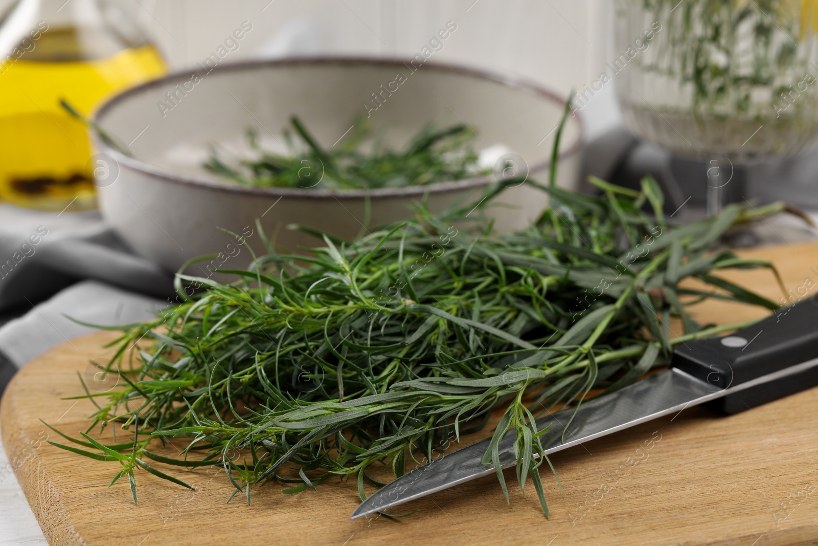 Photo of Fresh tarragon sprigs and knife on wooden board, closeup