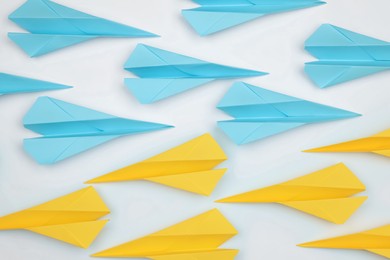 Photo of Handmade paper planes in light blue and yellow colors on white table, flat lay