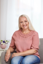 Photo of Portrait of beautiful older woman sitting on sofa indoors