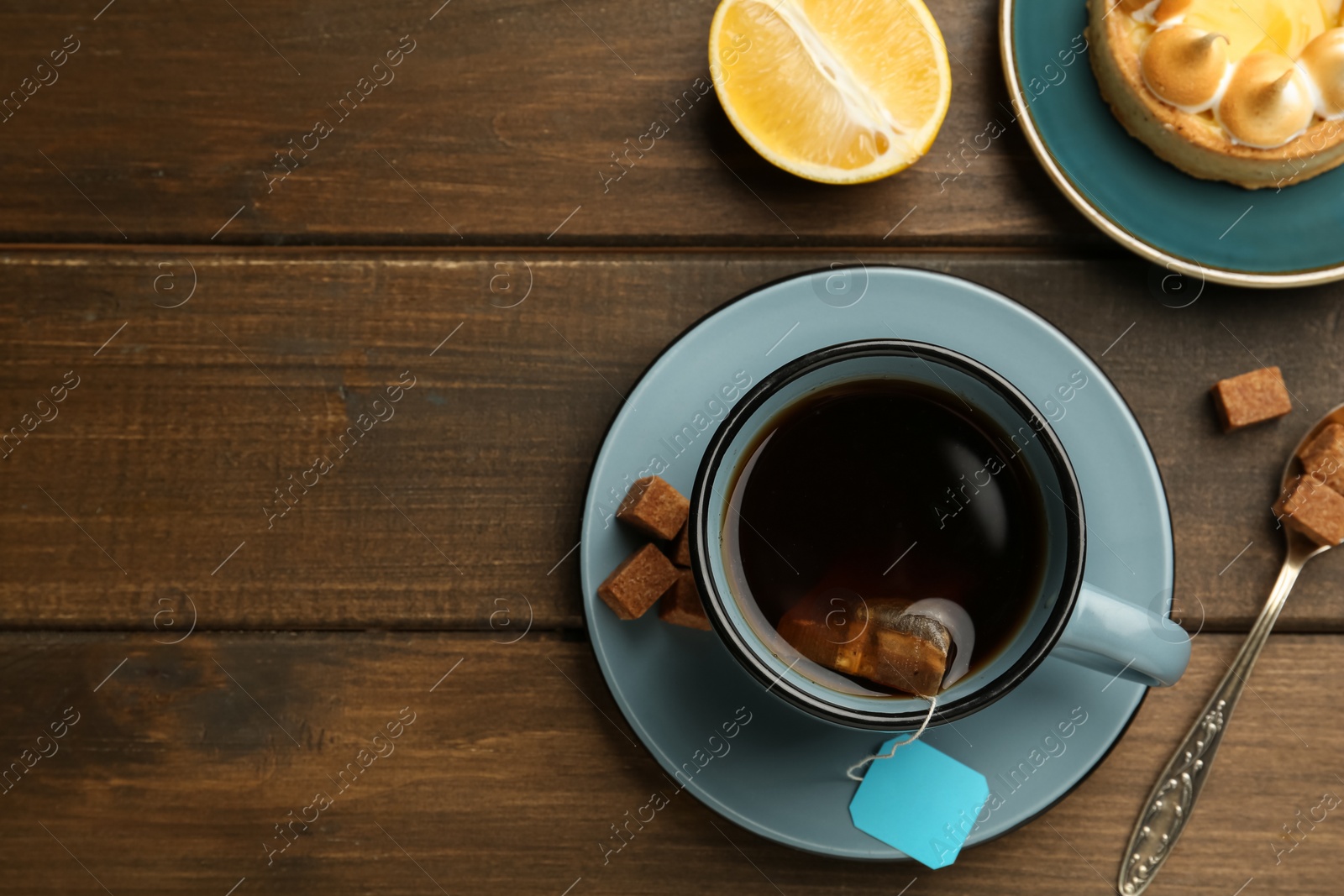 Photo of Tea bag in ceramic cup of hot water and sugar cubes on wooden table, flat lay. Space for text