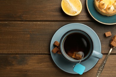 Photo of Tea bag in ceramic cup of hot water and sugar cubes on wooden table, flat lay. Space for text