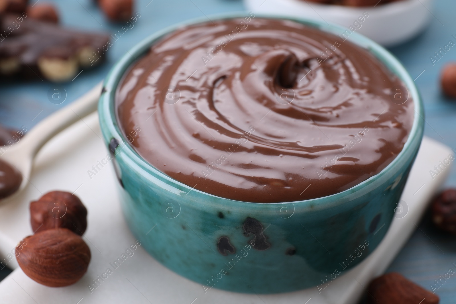Photo of Bowl with tasty chocolate paste and nuts on light blue wooden table, closeup