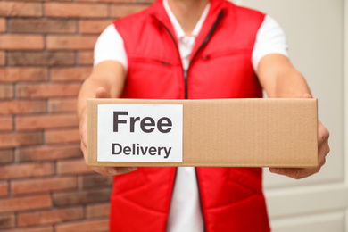 Photo of Courier holding parcel with sticker Free Delivery indoors, closeup