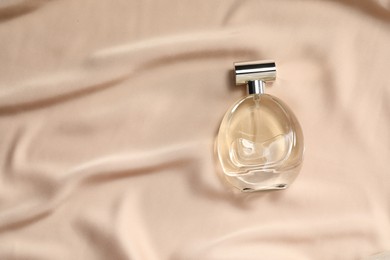 Photo of Luxury perfume in bottle on beige silk fabric, top view