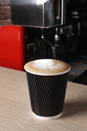 Photo of Takeaway paper cup of fresh aromatic coffee on wooden counter in cafe