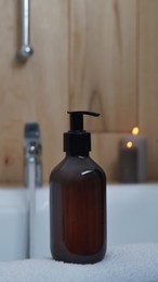 Photo of Black bottle of bubble bath and candles on tub indoors