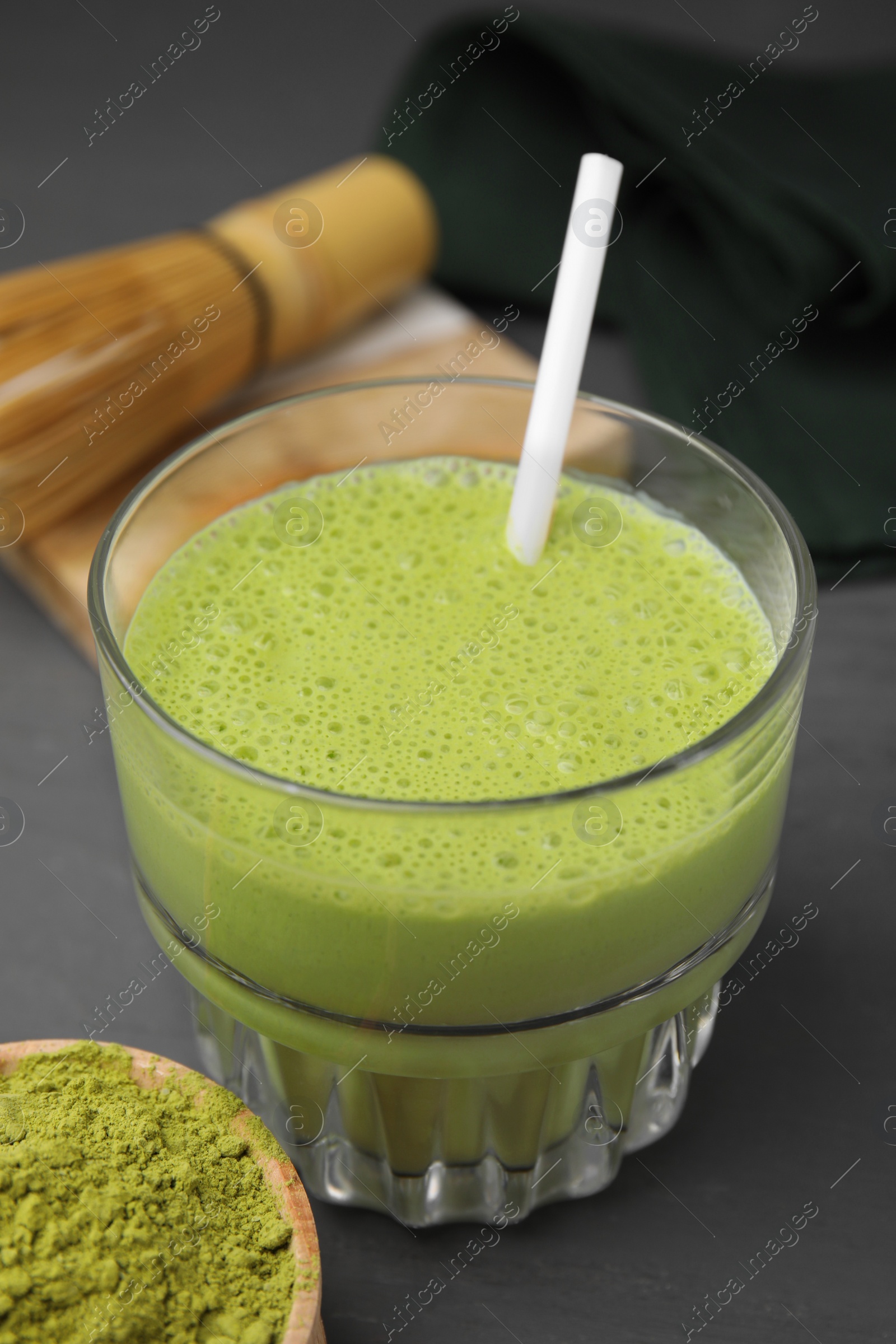 Photo of Glass of tasty matcha smoothie and powder on grey table, closeup