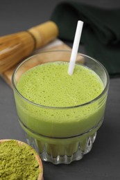 Glass of tasty matcha smoothie and powder on grey table, closeup