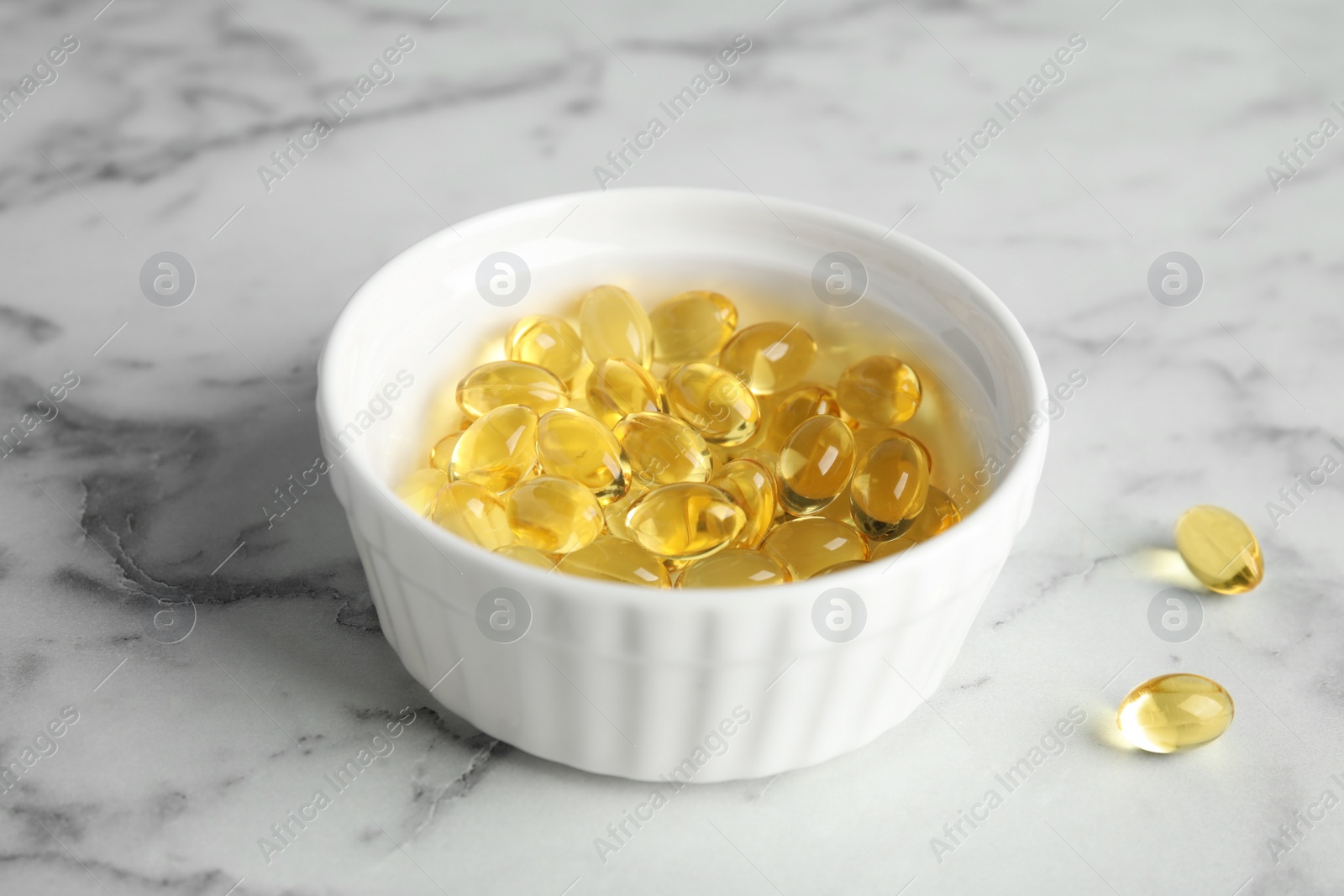 Photo of Bowl with cod liver oil pills on marble background