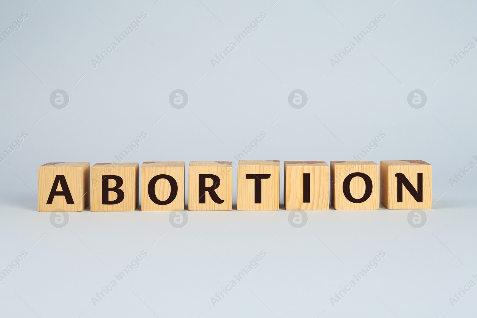 Photo of Word Abortion made of wooden cubes on light grey background