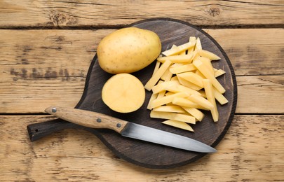 Photo of Whole and cut potatoes with knife on wooden table, top view. Cooking delicious french fries