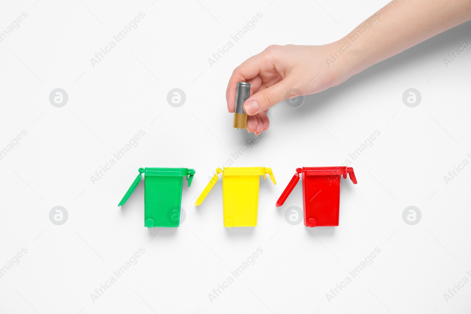 Photo of Woman throwing battery into trash bin on white background, top view