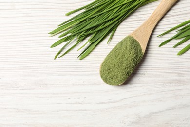 Wheat grass powder in spoon and fresh sprouts on white wooden table, flat lay. Space for text