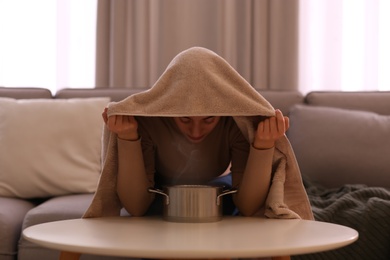 Woman with towel doing steam inhalation above pot at home