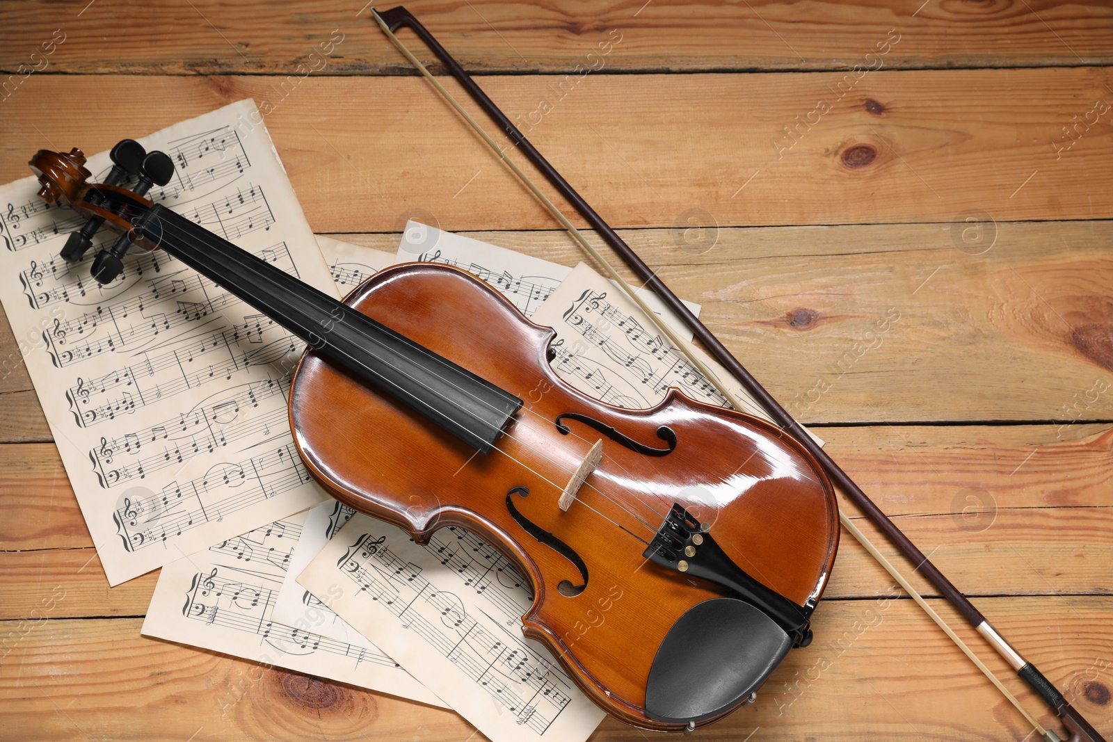 Photo of Violin, bow and music sheets on wooden table, top view