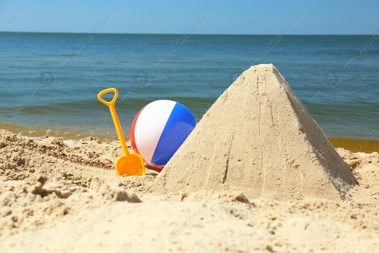 Photo of Sand pyramid, colorful ball and plastic shovel on beach near sea