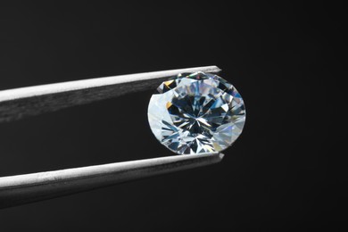 Tweezers with beautiful shiny diamond on black background, closeup