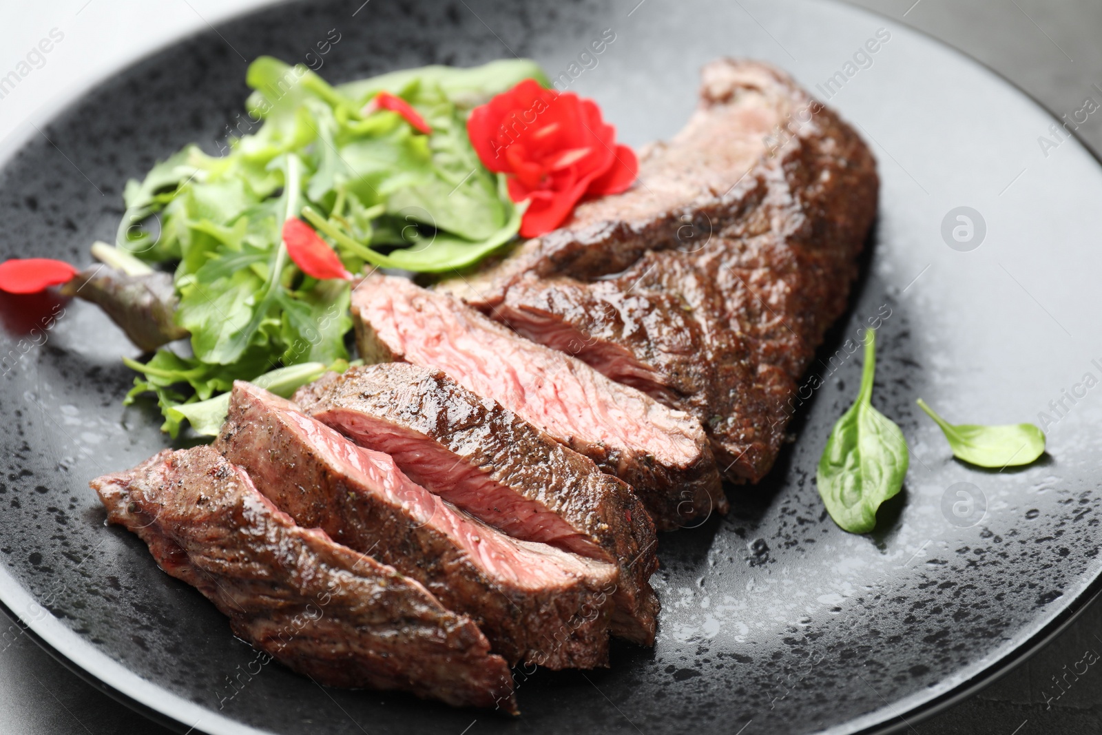 Photo of Pieces of delicious grilled beef meat and greens on table, closeup