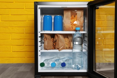 Mini bar filled with food and drinks near yellow brick wall indoors, closeup