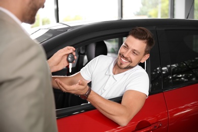 Photo of Salesman giving car key to customer in auto dealership