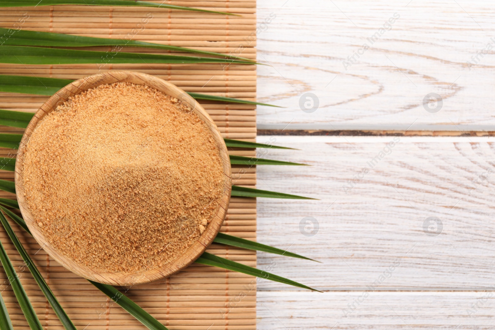 Photo of Coconut sugar, palm leaves and bamboo mat on wooden rustic table, top view. Space for text