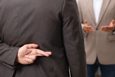 Photo of Employee crossing fingers behind his back while meeting with boss, closeup