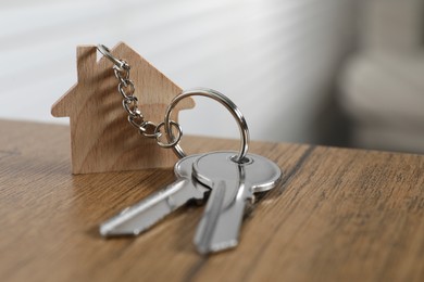 Photo of Keys with keychain in shape of house on wooden table against blurred background, closeup