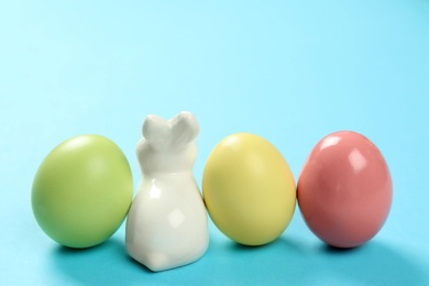 Ceramic Easter bunny and dyed eggs on color background