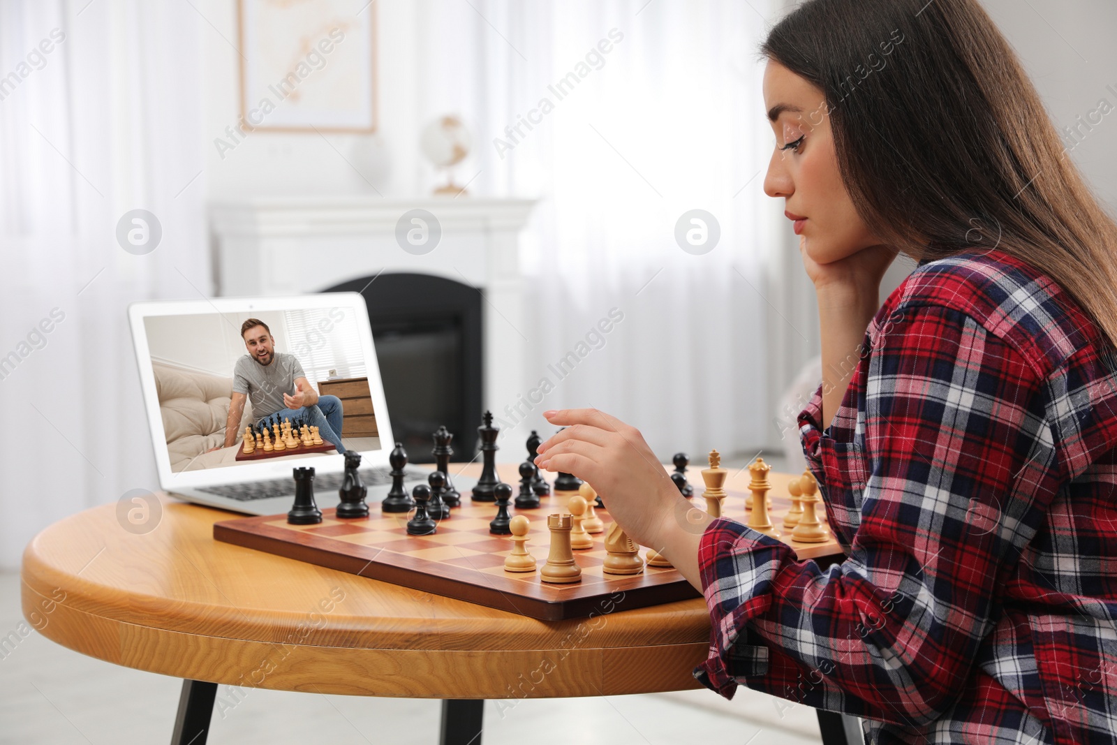 Image of Young woman playing chess with partner via online video chat at home