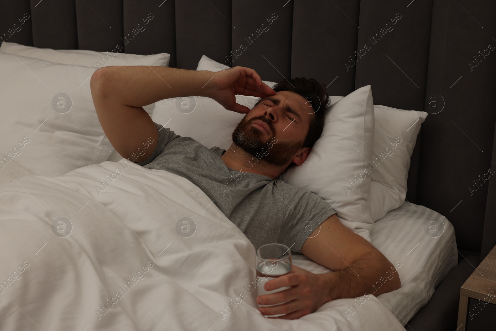 Photo of Man with glass of water suffering from headache in bed at night